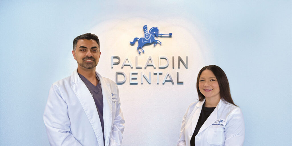 Two individuals wearing white lab coats standing in front of a wall with the text 'PALADIN DENTAL' and a knight on a horse logo.